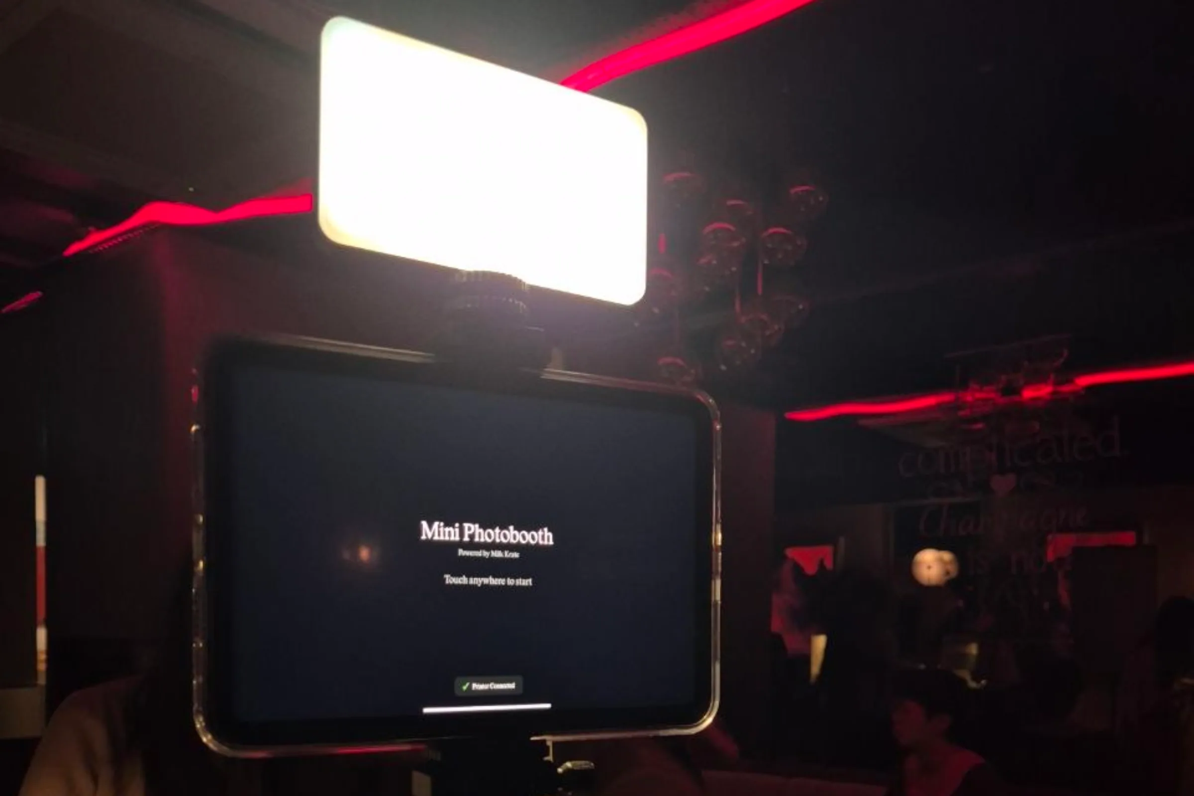 The booth's start screen in a dimly lit bar, reading Mini Photobooth, touch anywhere to start.